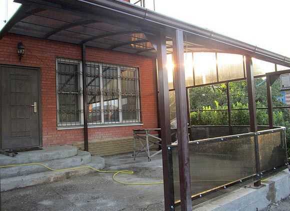 Une véranda en polycarbonate attachée à une maison en brique. L'ensemble du cadre est assemblé à partir d'un tube en forme